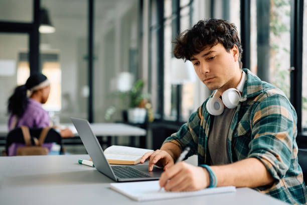 University student writing while using laptop and studying in the classroom. Copy space.